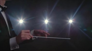 Müzisyenleri yöneten bir orkestra şefinin ellerini hareket ettirerek siyah arka planda ışıklar eşliğinde sopalarını hareket ettiriyorlar. Görünür jestlerle klasik müzik performanslarını yönetmek. Kapat..