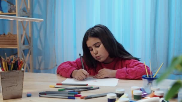 Klein schoolmeisje zit aan de tafel in de kamer en tekent met viltstiften in het album. Een tienermeisje is bezig met creativiteit, tekent een tekening. Sluit maar af. Slow motion klaar, 4K bij 59,94fps. — Stockvideo