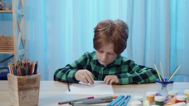 Liten skolpojke sitter vid bordet i rummet och ritar med penna i album. En tonårspojke är engagerad i kreativitet, tecknar en bild, hobby, utveckling. Närbild. Slow motion klar, 4K vid 59.94fps. — Stockvideo