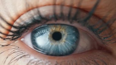 Mavi bir iris ve maskarayla boyanmış uzun kirpiklerle gözlerini açıp kapayarak. Gri göz, irisin, göz bebeğinin büyümesi ve büzülmesi. Göz küresi, retina, göz kapağı. Yavaş çekim.