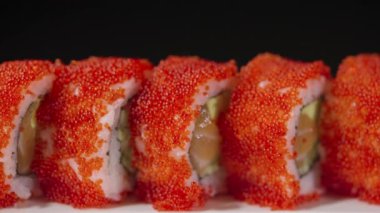 Kaliforniya suşisi, somon, avokado, salatalık ve siyah arka planda beyaz bir tabakta havyar. Geleneksel Japon yemekleri, Asya deniz ürünleri. Restoran sunumu. Suşi seti. Yavaş çekim.