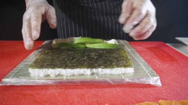Процес приготування суші-ролу Філадельфії закривається. Хуші мастер роздає рис, норі, сир і авокадо і перевертає його шматочками лосося. Традиційна японська кухня з морепродуктами та рибою. Так. Повільний рух. — стокове відео