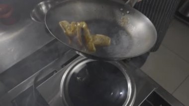 Asya restoranındaki bir restoranın şefi mutfağın arka planında sıcak tavada patlıcan pişiriyor. Bir adam sıcak baharat, sarımsak ve şeker şurubuyla yağda sebze kızartıyor. Ağır çekim. Kapat..