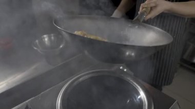 Asya restoranındaki bir restoranın şefi mutfağın arka planında sıcak tavada patlıcan pişiriyor. Bir adam sıcak baharat, sarımsak ve şeker şurubuyla yağda sebze kızartıyor. Ağır çekim. Kapat..