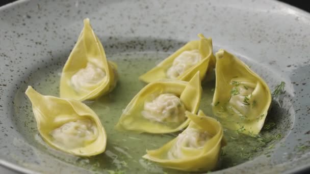 Chinesische Wonton-Knödel mit Dill und Gewürzen bestreut. Gefüllte Dampfknödel Dimm Sum in einem grauen Teller, der sich in Großaufnahme dreht. Asiatische traditionelle Suppe mit Wontons, gefüllt mit Fleisch. Zeitlupe. — Stockvideo