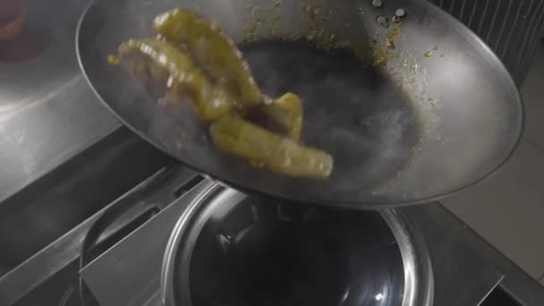 Chef de um restaurante asiático frita berinjela em uma frigideira quente no fundo da cozinha. Um homem frita legumes em óleo com especiarias quentes, alho e xarope de cana-de-açúcar. Movimento lento. Fechar. — Vídeo de Stock