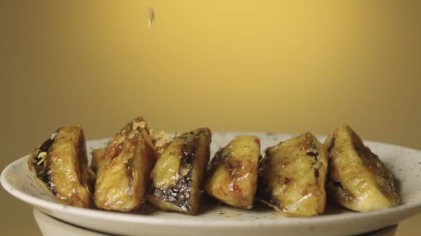 Πιάτο με φρυγανισμένες καραμελωμένες μελιτζάνες με πικάντικα μπαχαρικά και τραγανό γλάσο πασπαλισμένο με νιφάδες, κοντά σε καφέ φόντο. Τραγανά κομμάτια μελιτζάνας τηγανισμένα σε λάδι με σκόρδο. Ασιατική κουζίνα. Αργά — Αρχείο Βίντεο
