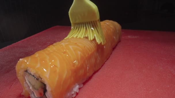 Filadelfia rollo de sushi con salmón se unta con salsa usando cepillo culinario. Cocinar comida tradicional japonesa con mariscos y pescados. Cocina asiática. Restaurante o bar de sushi. De cerca. Movimiento lento. — Vídeos de Stock