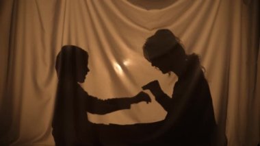 Kadın ve çocuğun gölgelerle oynayarak, sarılarak ve sevinerek hikâyeler anlattığı siluetler. Anne ve küçük oğlu evde, perdenin arkasında oturarak eğleniyor. Gölgeler kukla tiyatrosu. Kapat..