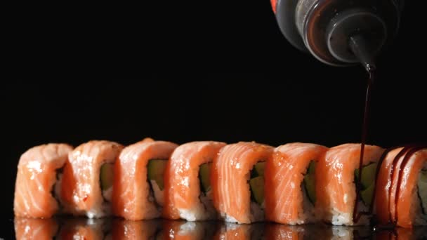 Sushi master menuangkan saus unagi di atas Philadelphia roll. Sushi roll dengan salmon, nasi, alpukat dan keju. Memasak makanan tradisional Jepang dengan makanan laut dan ikan. Tutup set sushi. Gerakan lambat. — Stok Video