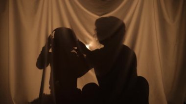 Büyük kulaklıklarla müzik dinleyen kadın ve çocuk siluetleri. Anne ve oğlu evde perdenin arkasında birlikte vakit geçiriyorlar. Gölgelerin kukla tiyatrosu, gölge ve ışığın oyunu. Kapat..