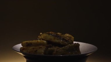 Tempura patlıcan dilimleri ve gri tabakta dönen baharatlar. Yağda kızartılmış çıtır patlıcan parçaları, parlak ışık ve karanlıkta çekilmiş. Baharatlı sebze servisi yapan bir restoran. Yavaş çekim.