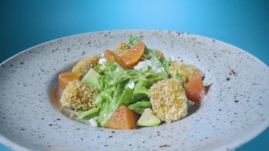 Greyfurtlu salata, yeşil marul, avokado, ton balığı ve peynir gri tabakta, mavi arka planda dönüyor. Restoran yemeği. İtalyan salatası. Fransız mutfağı. Yavaş çekim.