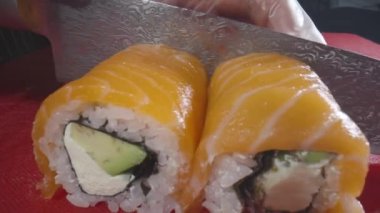 Philadelphia usulü suşi pişirme işlemi yakın çekim. Suşi ustası ruloyu keskin bir bıçakla parçalara ayırıyor. Geleneksel Japon yemekleri ve deniz ürünleri. Asya mutfağı. Suşi seti. Yavaş çekim.