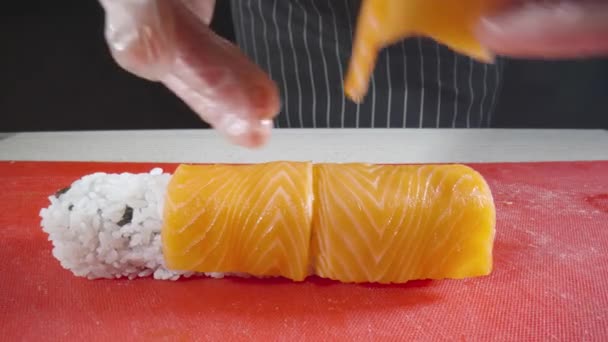 Proceso de cocinar rollos de sushi Filadelfia de cerca. El maestro del sushi cubre el rollo con rodajas de salmón y lo aprieta con una estera de bambú. Comida tradicional japonesa con mariscos y pescados. Movimiento lento. — Vídeos de Stock