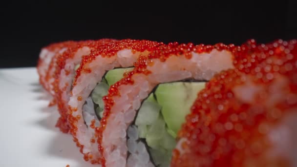 Kalifornien sushi rulle med ris, lax, avokado, gurka och kaviar på en vit platta på en svart bakgrund. Traditionell japansk mat, asiatiska skaldjur. Restaurangpresentation. Sushi-inspelning. Långsamma rörelser. — Stockvideo