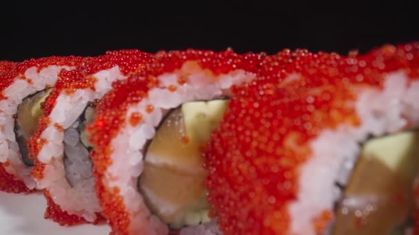 California sushi roll dengan nasi, salmon, alpukat, mentimun dan kaviar pada piring putih di latar belakang hitam. Makanan tradisional Jepang, makanan laut Asia. Restoran presentasi. Sushi siap. Gerakan lambat. — Stok Video