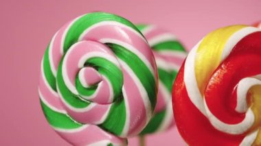 Pembe arka planda dönen yuvarlak karamelli lolipoplar. Meyve aromalı çeşitli tatlı şekerler. Çocukların doğum günü için tatlı. Yavaş çekim hazır, 4K 59.94 fp 'de. Kapat..