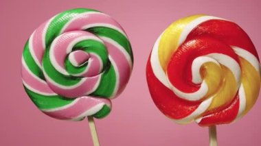 Kamera, pembe arka planda kıvrılmış karamel lolipopların üzerinde kayıyor. Meyve aromalı renkli çizgili tatlı şekerler. El yapımı tatlılar. Yavaş çekim hazır, 4K 59.94 fp 'de. Kapat..