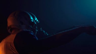 Amerikan futbolu oynamaya hazır üniformalı ve kasklı iki kararlı sporcunun yan görüntüsü. Kendinden emin ve agresif oyuncular karanlık arenada ışıklarla dururken rakiplerine meydan okuyorlar. Kapat..
