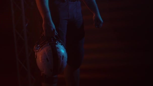 Porträtt av en skäggig amerikansk fotbollsspelare som står i en mörk arena med ljus och rök och håller i en hjälm. Självsäker och aggressiv man i uniform. En maskulin fotbollsspelare. Kraftspel. Närbild. — Stockvideo