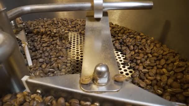 工場内の工業用コーヒー焙煎機での焙煎工程。焙煎したコーヒー豆を混ぜる。芳香族茶色の豆を閉じる渦巻く。カフェのための食べ物や飲み物の背景。スローモーション. — ストック動画