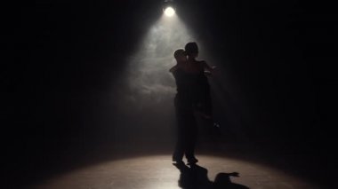 Kadın ve erkek karanlıkta üstlerinde ışık ve dumanla Latin dansı yapıyorlar. Karanlık arka planda tutkuyla dans eden iki dansçının siluetleri. Yavaş çekim hazır, 4K 59.94fps 'de..