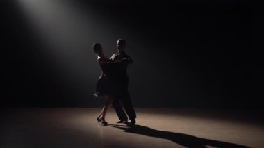 Çift dansçılarının silueti karanlıkta dumanla ve spot ışıklarıyla tango yapıyor. Bir çift balo dansçısı. Latin Amerika dansları okulunda koreografi dersi. Yavaş çekim hazır, 4K 59.94fps 'de..