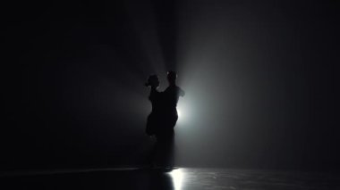 Arjantin tangosu iki dansçı tarafından icra edildi. Karanlıkta arka plan ışığı ve dumanla dans eden kadın ve erkeğin siluetleri. Yavaş çekim hazır, 4K 59.94fps 'de..