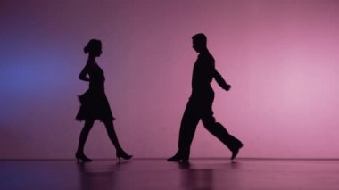 İki dansçı birbirlerine yaklaşıp tango yapmaya başlıyorlar. Stüdyoda latin dans koreografisi unsurları mavi pembe arka planda. Koyu renk siluetler. Yavaş çekim hazır, 4K 59.94fps 'de..