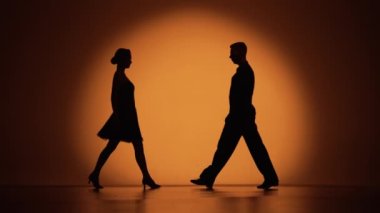 İki dansçı birbirlerine yaklaşıp Arjantin tangosu yapmaya başlarlar. Latince balo dansı elementleri stüdyoda turuncu kahverengi arka planda. Koyu renk siluetler. Yavaş çekim hazır, 4K 59.94fps 'de..