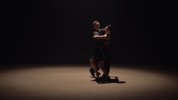 Пара виконує емоційний танець у темряві з заднім світлом. Танець з аргентинського танго. Урок з хореографії в школі танців. Повільний рух готовий, 4К на 59,94fps. — стокове відео