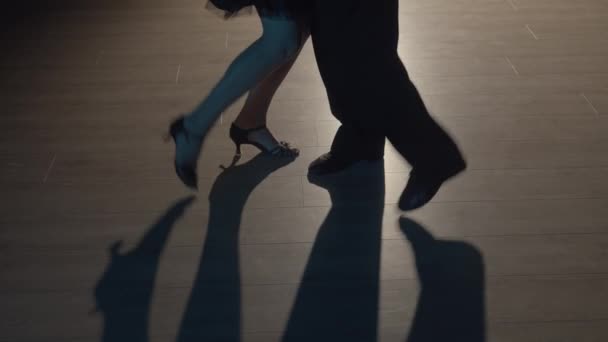 Duas pernas a fazer passos de dança latina no chão. Parceiros desconhecidos dançando coreografia tango argentino. Homem e mulher dançam no escuro com luz de fundo. Fecha. Movimento lento pronto, 4K a 59.94fps. — Vídeo de Stock