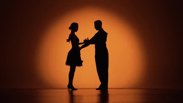 Några dansare närmar sig varandra och börjar dansa argentinsk tango. Delar av latinska balsal dans i studio med orange brun bakgrund. Mörka silhuetter. Slow motion klar, 4K vid 59.94fps. — Stockvideo