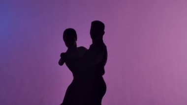 Arjantin tangosu iki dansçı tarafından icra edildi. Stüdyoda pembe arka planı olan Latin dansı koreografisi yapan kadın ve erkeğin siluetleri. Kapatın. Yavaş çekim hazır, 4K 59.94fps 'de.