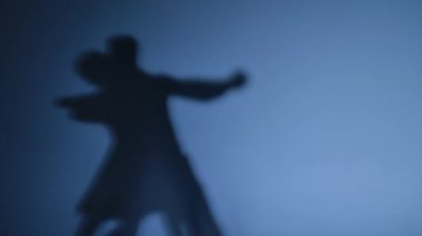 Dansçıların dans eden gölgeleri mavi stüdyo arka planında Arjantin tangosu yapıyorlar. Erkek ve kadın, Latin koreografisinin unsurlarını uyguluyor. Kapatın. Yavaş çekim hazır, 4K 59.94fps 'de..