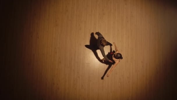 Vista superior de um par de dançarinos de salão dançando elementos de tango argentinos em um piso de parquet. Movimentos apaixonados de parceiros na dança latina em um fundo marrom. Movimento lento pronto, 4K a 59.94fps — Vídeo de Stock