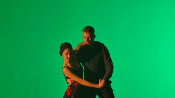 Чоловік в костюмі і жінка в чорному короткому вбранні виконують латинський танець на зеленому фоні студії. Пара танцюристів пристрасно танцює аргентинське танго. Закрийся. Повільний рух готовий, 4К на 59,94fps. — стокове відео