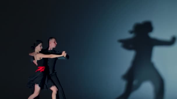 Dança de tango realizada por dois dançarinos de salão. Homem e mulher praticam elementos da coreografia latina. Tiros contra fundo cinzento com sombras dançantes. Fecha. Movimento lento pronto, 4K, 59.94fps. — Vídeo de Stock