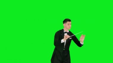 Takım elbiseli senfoni orkestra şefi, stüdyodaki yeşil ekranda izole edilmiş baton hareketiyle müzisyenleri yönetiyor. Görünür jestlerle müzik performanslarını yönetmek. Kapat..