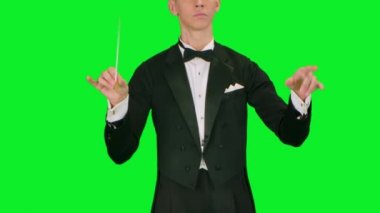 Orkestra şefi batonunu stüdyodaki yeşil ekranda müzisyenleri yönetmek, senkronize etmek ve yönetmek için sallıyor. Hareketli el hareketleriyle klasik müzikal performans. Kapat..
