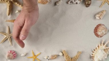 Mans el kumu temizliyor reklam alanını gösteriyor, çalışma alanı modelleniyor. Deniz kabukları ve deniz yıldızlarıyla dolu kumlu bir arka plan. Tatil ya da seyahat reklamı için. Kapat..