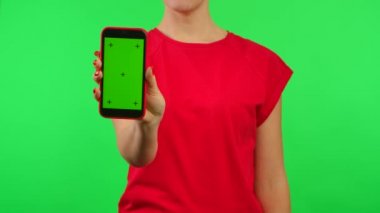 Kırmızı tişörtlü kadın ellerini tutuyor ve çalışma alanı yeşil arkaplanlı cep telefonunu gösteriyor. Reklam alanı. Metin veya resim için şablon yeri, promosyon içeriği. Kapat..