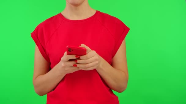 Vrouw in rood tshirt sms 'en op smartphone en demonstreert telefoon met werkruimte mock up scherm op groene achtergrond. Vrouwelijke vinger wijst naar informatie op het display. Reclamegebied. Sluiten.. — Stockvideo