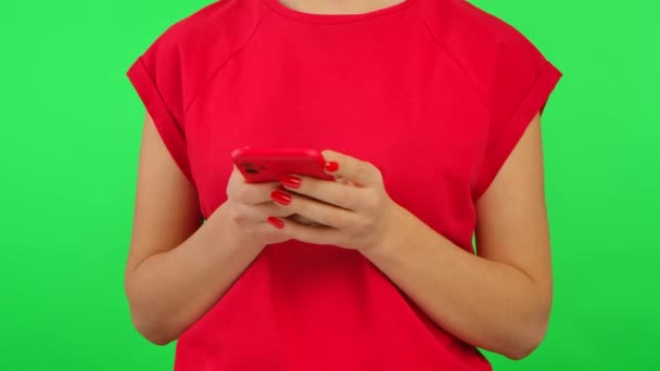 Vrouw in rood tshirt sms 'en op haar smartphone op groen scherm chroma key achtergrond. Onherkenbare vrouw is communicatie op online chat sociaal netwerk. Sluiten.. — Stockvideo