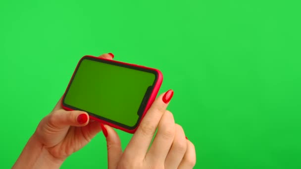 Weibliche Hand hält Mobiltelefon mit Arbeitsplatz-Attrappe auf grünem Hintergrund in horizontaler Position. Frau berührt Bildschirm, klickt und surft Inhalte im Internet. Werbefläche. Nahaufnahme. — Stockvideo