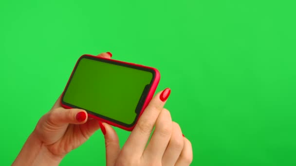 Vrouwelijke hand houdt mobiele telefoon met werkruimte mock up scherm op groene achtergrond in horizontale positie. Vrouw raakt scherm, klikt en bladert inhoud op internet. Reclamegebied. Sluiten.. — Stockvideo