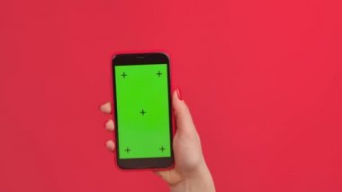 Yeşil çalışma alanı olan bir kadın cep telefonu kırmızı stüdyo arka planında ekran görüntüsü oluşturur. Kadın dokunmatik ekrana tıklayarak internet içeriğine göz atıyor. Reklam alanı. Şablon yeri. Kapat..