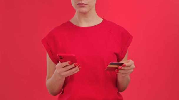 Vrouw doet een online aankoop met een creditcard en smartphone met groene werkruimte mock up scherm op rode achtergrond. Reclamegebied. Template plaats voor tekst of afbeelding, promotionele inhoud. Sluiten — Stockvideo