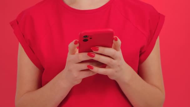 Donna irriconoscibile scrive messaggi di testo sul suo smartphone su uno sfondo rosso studio. Giovane donna comunica in chat online social network, fa acquisti, sfoglia i contenuti su internet. Da vicino.. — Video Stock